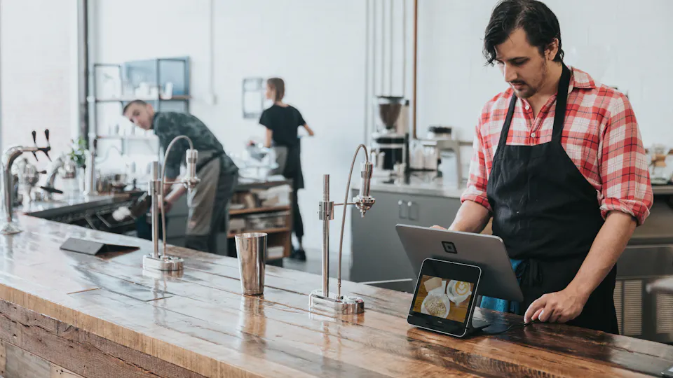 A barista using a tablet at the counter of a coffee shop