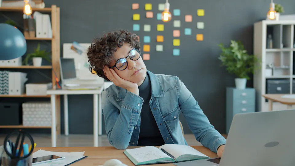 A tired person resting their head on one hand at a desk