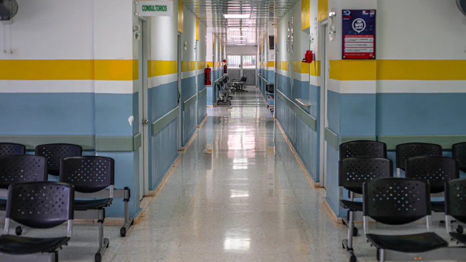 A long hospital corridor with chairs and a clock on the wall
