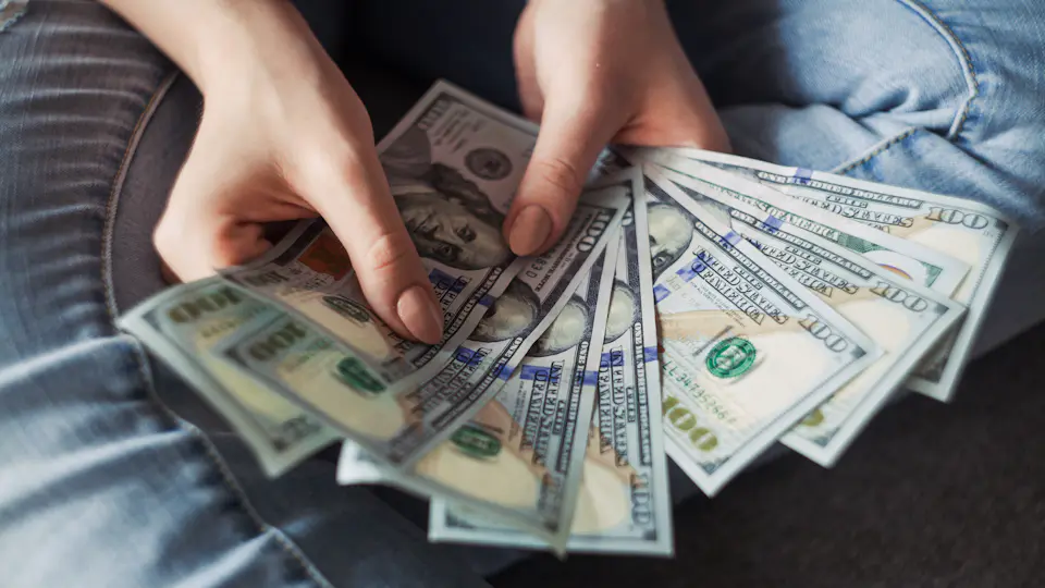 Hands fanning out a stack of 100-dollar bills