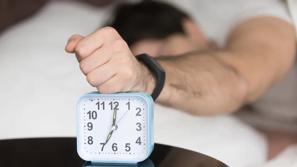 A man lying in bed holding an alarm clock