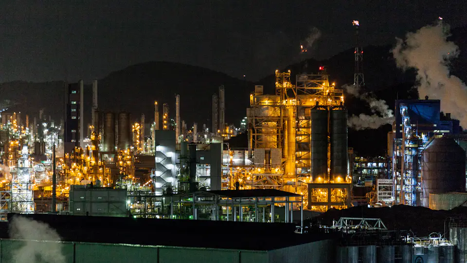 An industrial plant lit up at night, with steam rising from its towers