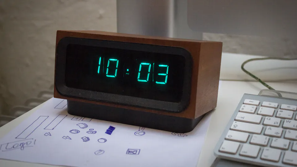 A digital desk clock next to a keyboard on an office desk
